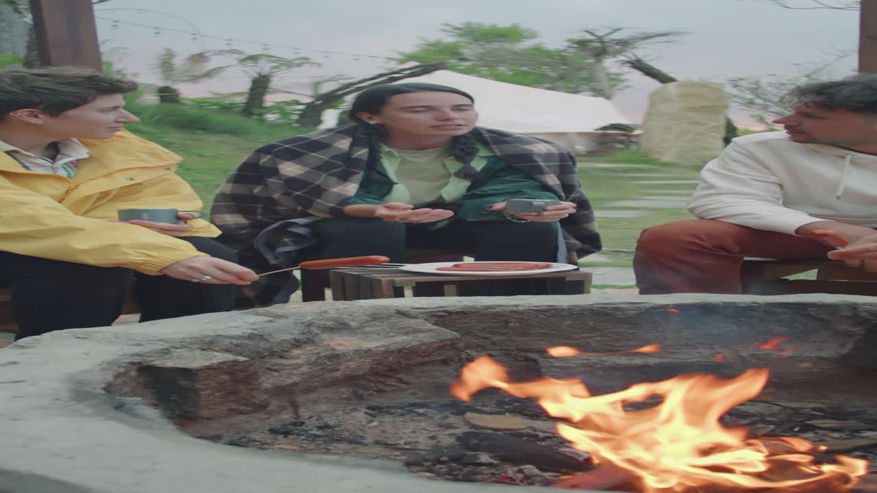 Company of Tourists Resting by Campfire at Glamp