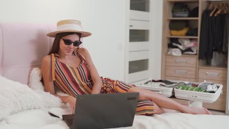 hermosa chica en una tarjeta en la cama elige en una laptop dónde volar de vacaciones, en el fondo de una maleta recolectada
