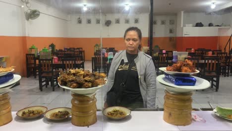 asian woman in &quot;berkah dalem&quot; or god bless t-shirt is choosing a food in padang stall