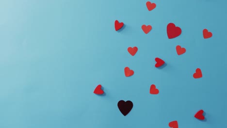 múltiples corazones de papel rojo y negro en el día de san valentín sobre un fondo azul