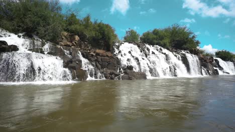 Niedrige-Kamerafahrt-Mit-Blick-über-Das-Wasser-An-Den-Mocona-Wasserfällen-Mit-Blauem-Himmel,-Brasilien