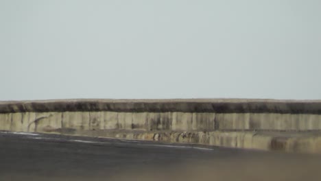 vista en ángulo bajo de dos cubanos en una motocicleta que pasa por la famosa carretera oceánica llamada malecón en la habana en un día soleado mientras la neblina de calor asciende visiblemente desde el asfalto