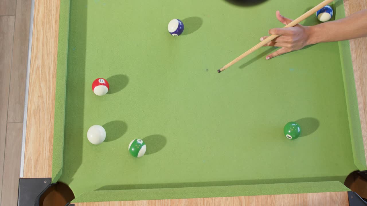 Hand is entering frame, aiming cue, striking cue ball and sinking green ball into corner pocket