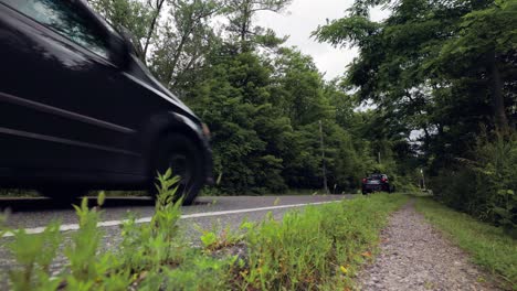 vista de ángulo bajo desde el lado de una carretera estrecha con autos en movimiento rápido rodeados de bosques y árboles y cielos grises