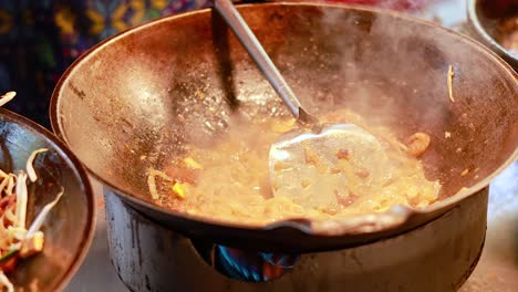 stir-frying pad thai noodles in a hot wok