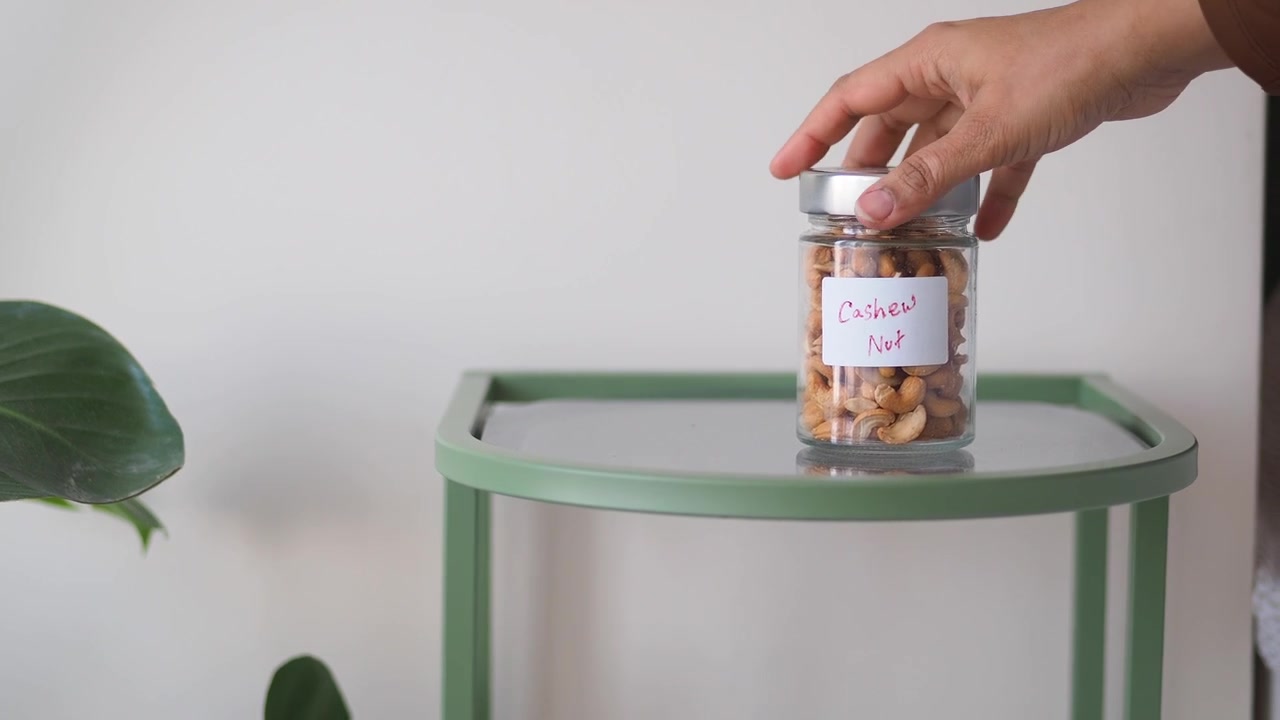 Hånd tager et glas med cashewnødder fra et bord