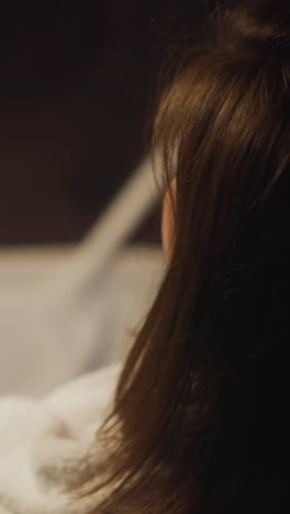 brunette woman dressed in white bathrobe relaxes relishing hot coffee in dimly lit living room. lady focuses on thoughts sitting alone in tranquil atmosphere