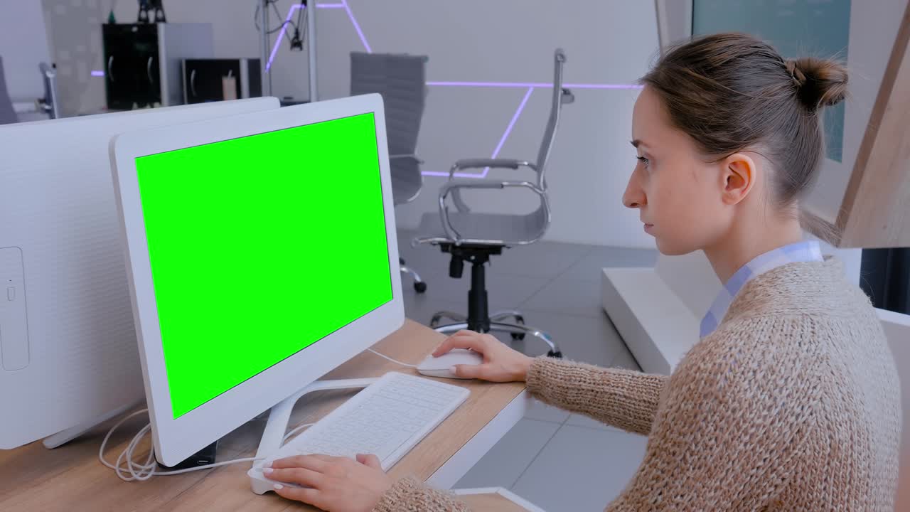 Woman looking at white monitor of desktop computer with blank green display