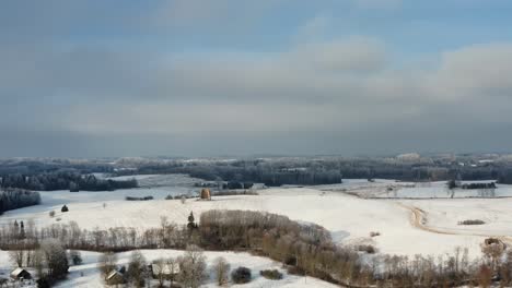 drone shot of ancient windmill ruins on a snowy hilltop, surrounded by a frozen winter forest under the glowing sun. aerial view over countryside landscape in winter.