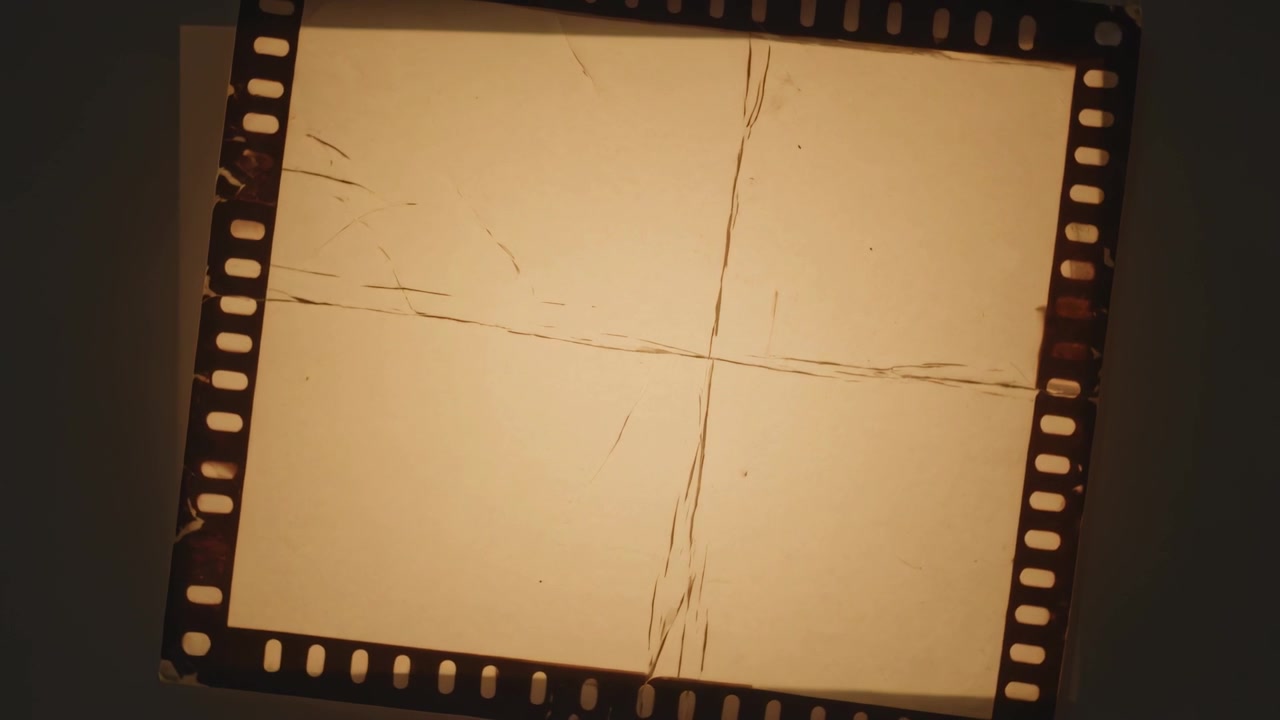 Marco de película de 35 mm girando después de colocarlo en una mesa de luz en el escritorio, mostrando perforaciones y marcas de cruz para escanear.