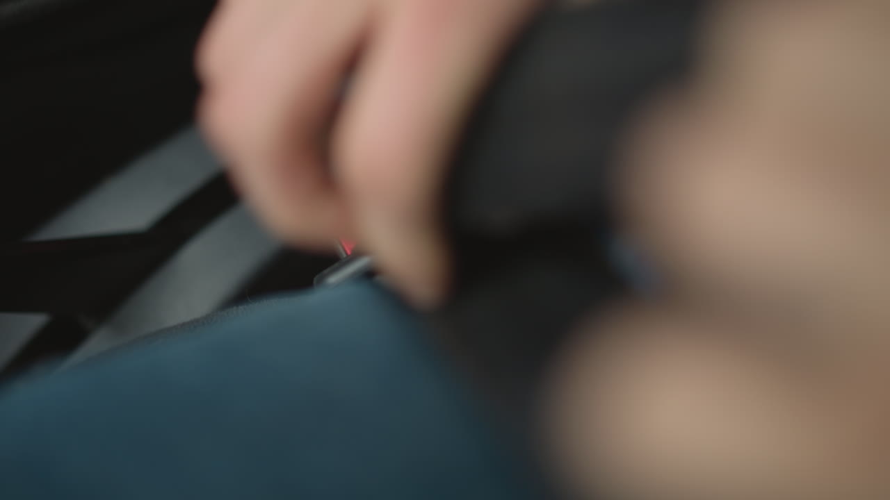 High angle view of road explorer wearing seat belt inside car seat, black puffer jacket visible, urban backdrop through window, focus on belt over blue jeans and protective posture before journey