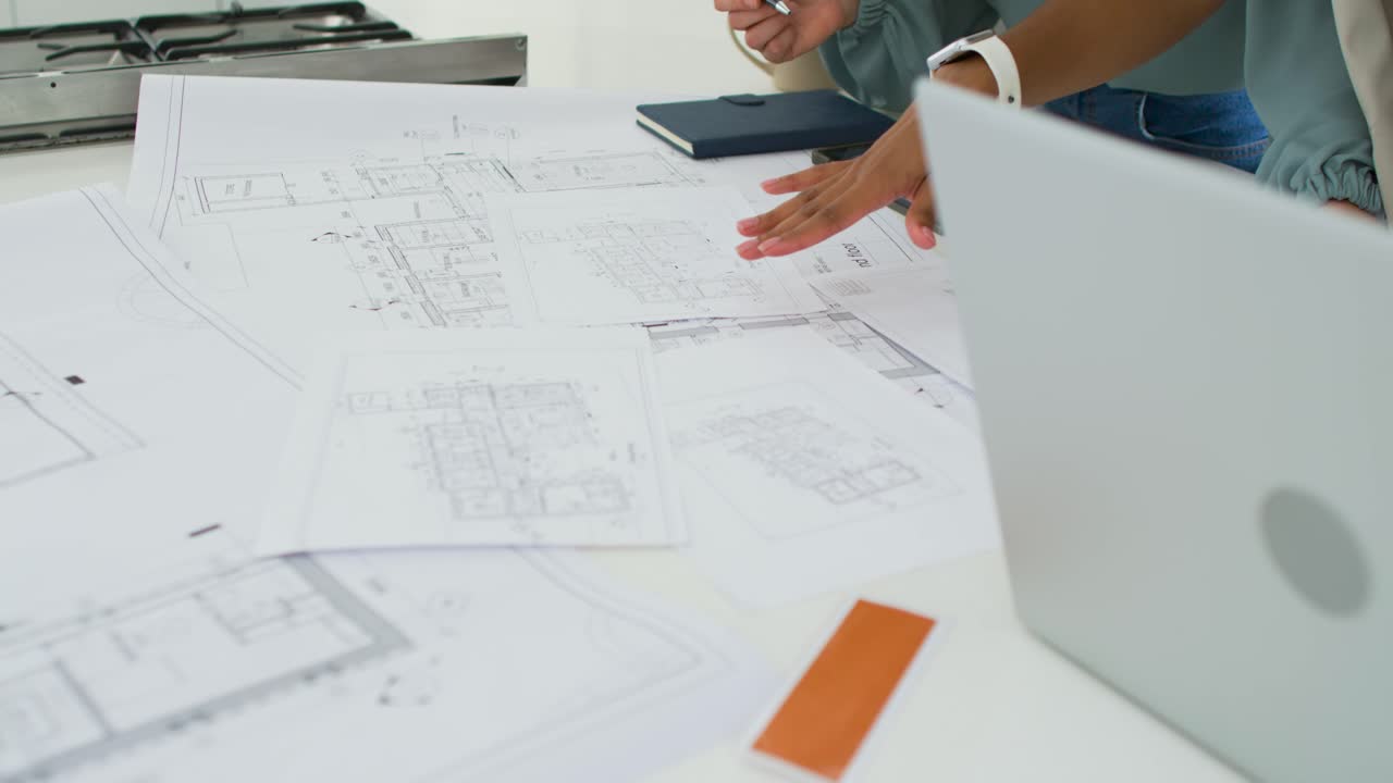 Female team working on design after opening laptop, reviewing blueprints on studio table, pointing