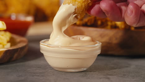 hand dipping fried chicken nuggets in creamy sauce