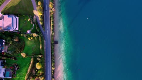 Vista-Aérea-Panorámica-De-Un-Camino-Sinuoso-Bordeado-De-árboles,-Que-Conduce-A-Un-Lago-Azul