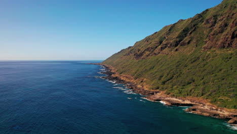 Beautiful-blue-waves-by-the-green-mountains-of-West-Oahu,-Hawaii---aerial