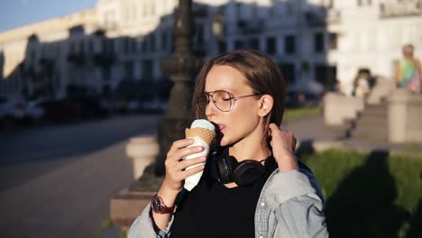 mujer joven con camisa naranja disfrutando de helado de vainilla suave en cono de gofres al aire libre en cámara lenta. mujer tomando y helado