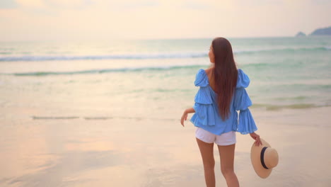 back view of woman walks on seashore and raises her arms