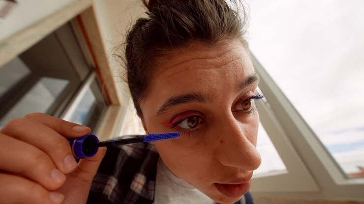 Giovane donna che applica mascara blu sulle ciglia