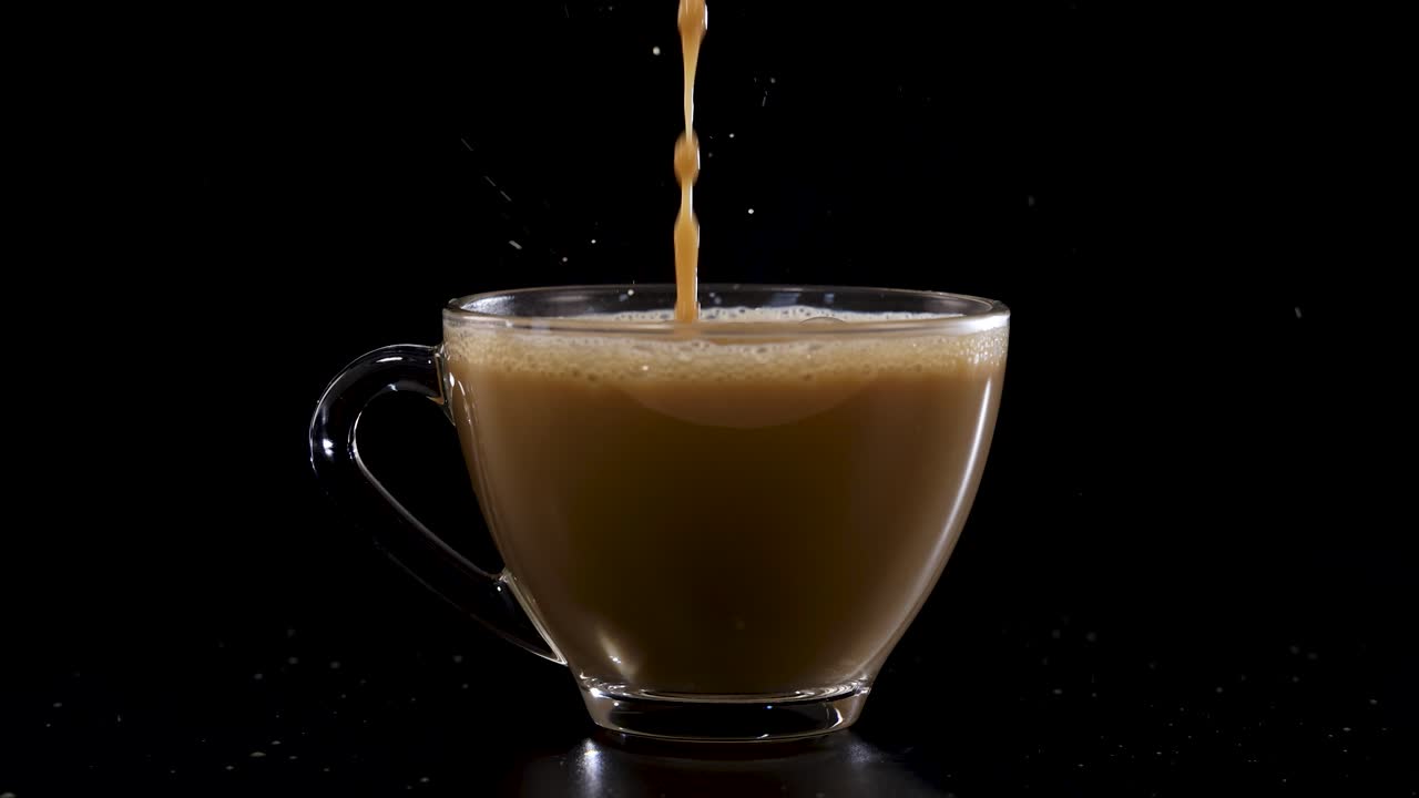 Coffee is poured into a glass cup against a black background, captured in slow motion with dramatic lighting