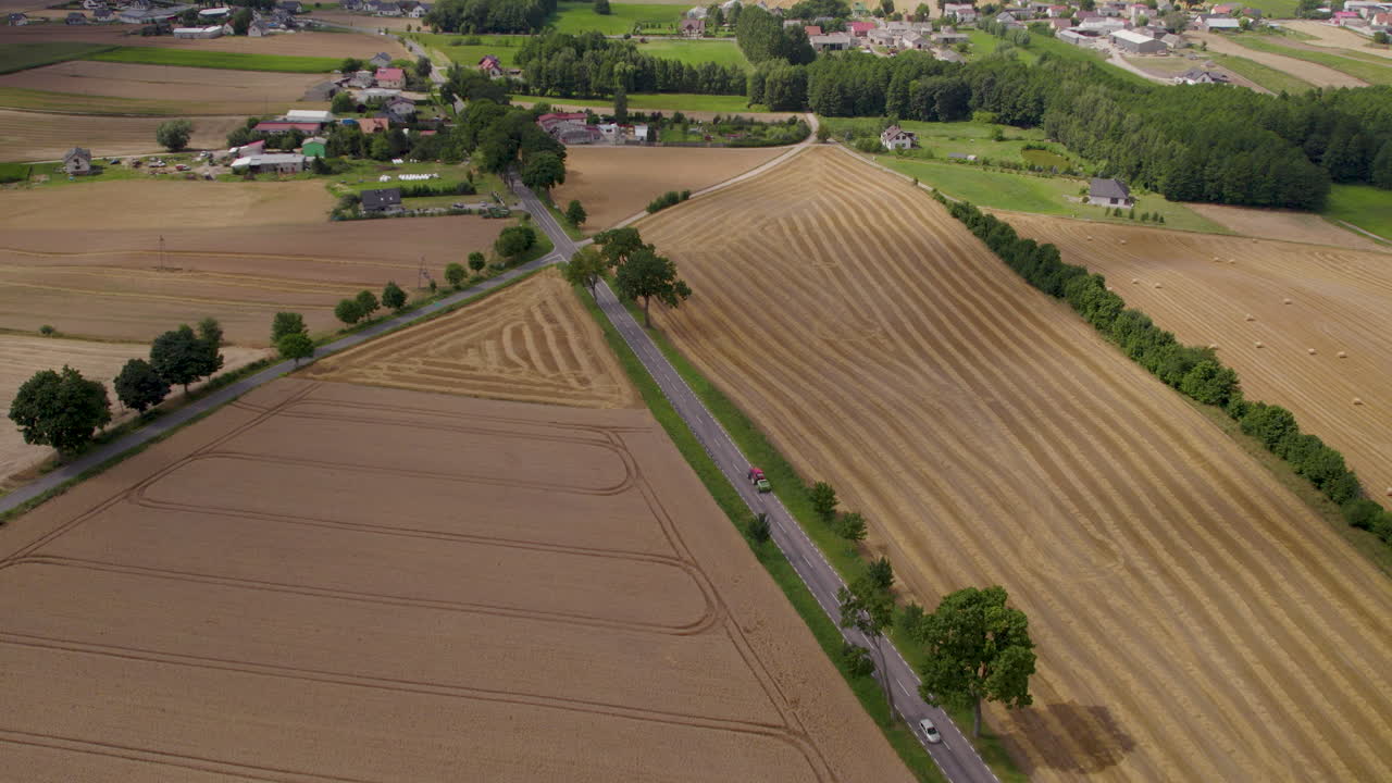 수확된 들판이 있는 폴란드의 시골 도로에서 건초 더미를 운반하는 캐리어가 있는 트랙터 - 공중 추적 필드