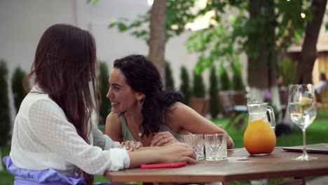 people, communication and friendship concept - smiling young women drinking, talking at outdoor cafe, brunette sharing good news