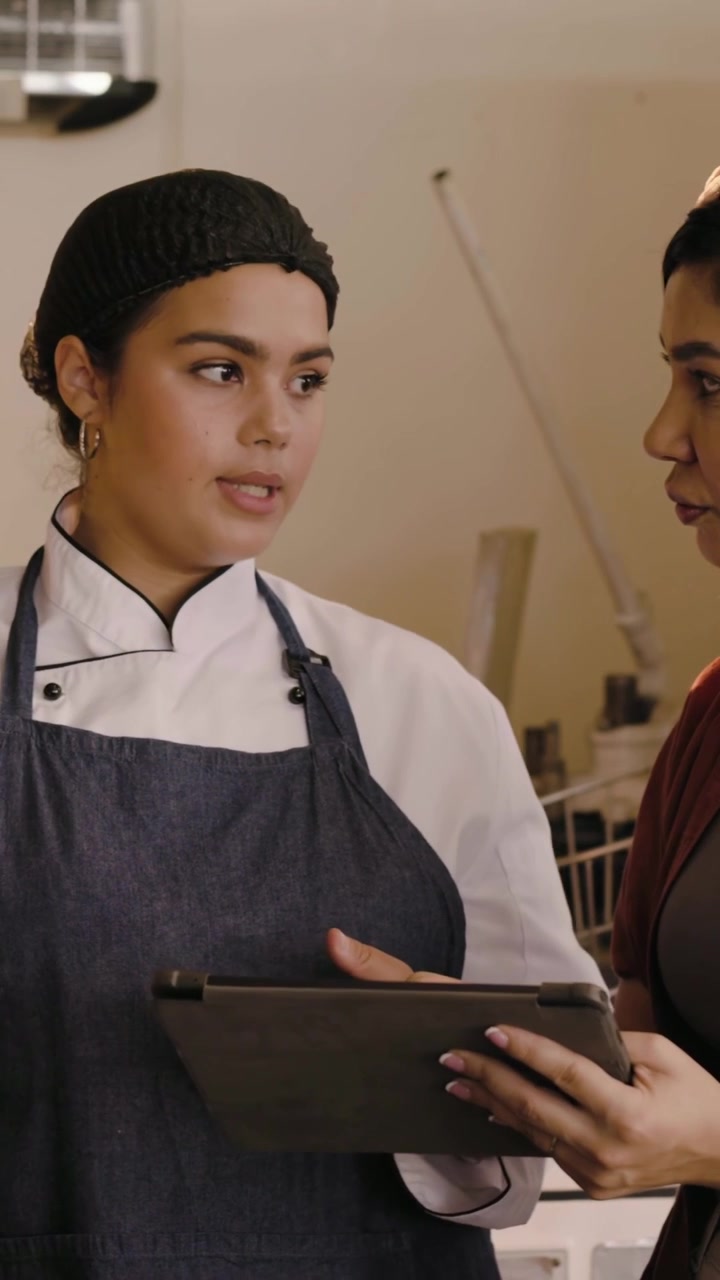 Vertikal video: Tager tablet fra leder, kok i jakke trykker på skærm og gennemgår menu i køkken