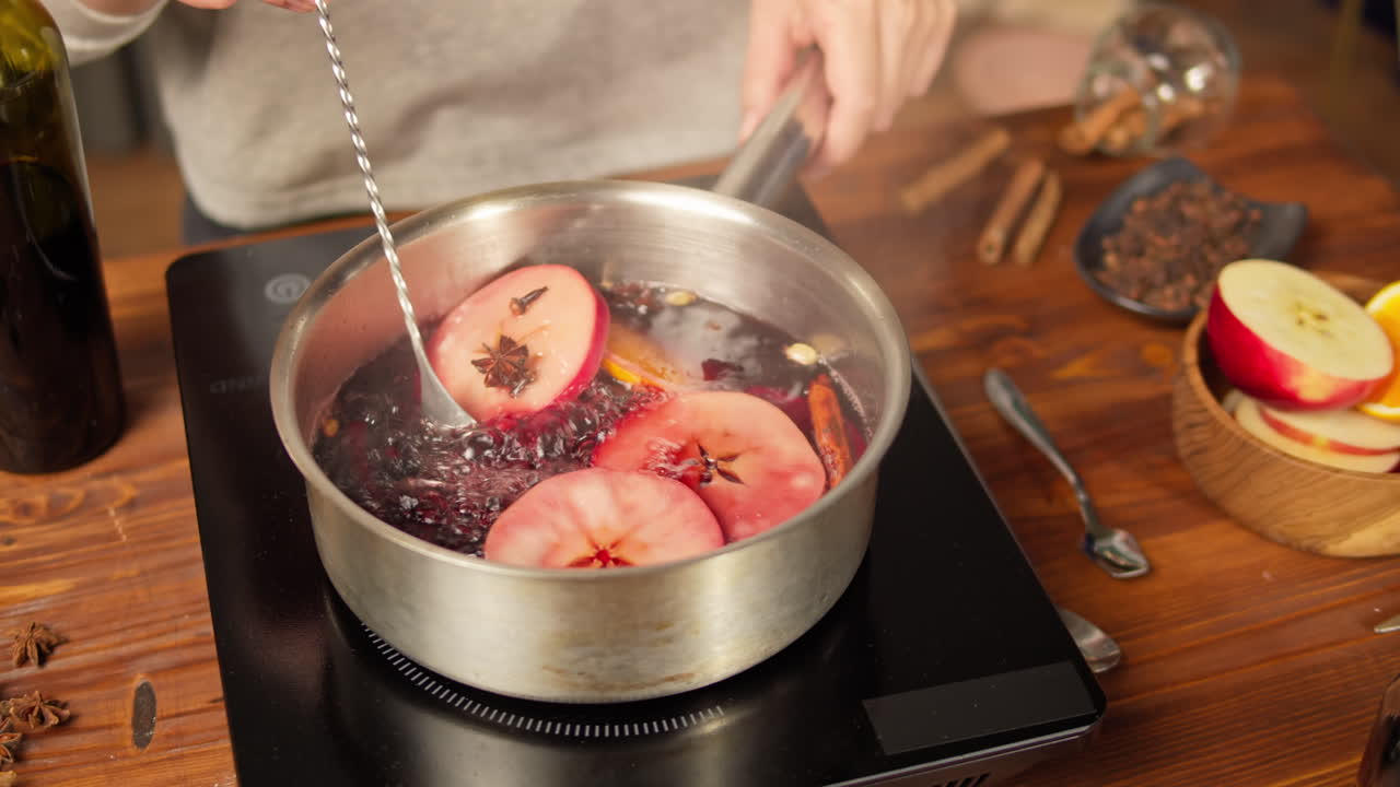 Mescolando il vin brulé con mele e spezie in una pentola.