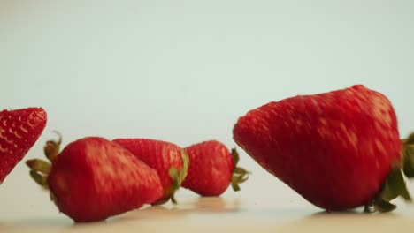 Dramatic-fresh-fruit-shot-of-a-bunch-of-big-bright-red-strawberries-dropping-from-the-top,-rolling-off-the-scene,-studio-health-food-detox-concept-shot