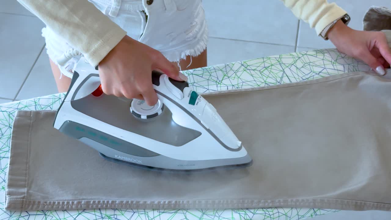 A person irons pants on a board in a well-lit room, focusing on smooth, precise movements