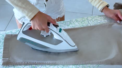 a person irons pants on a board in a well-lit room, focusing on smooth, precise movements