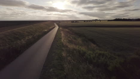 fast drone flight forward above an empty dyke road, back light, scenic landscape, sunset, sky with scenic clouds