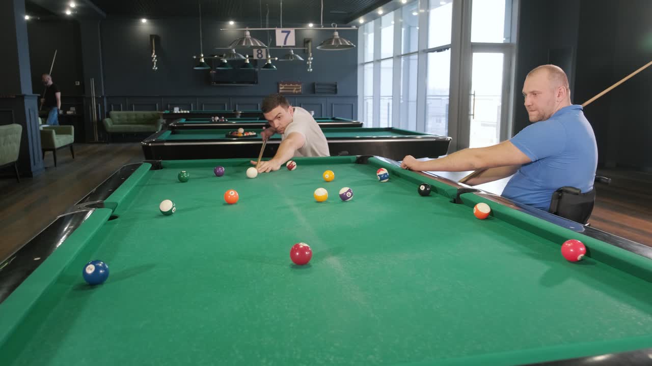 Adult men with disabilities in a wheelchair play billiards in the club