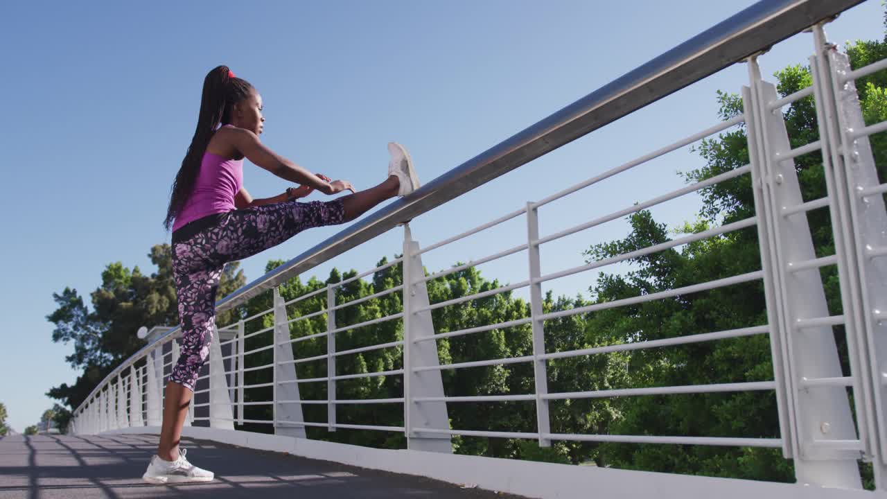 mujer afroamericana estirando su pierna en la barandilla del puente de la ciudad