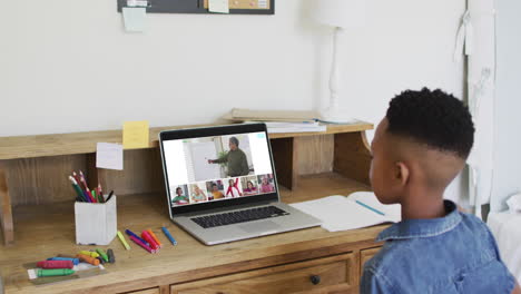 schoolboy using laptop for online lesson at home, with diverse teacher and class on screen