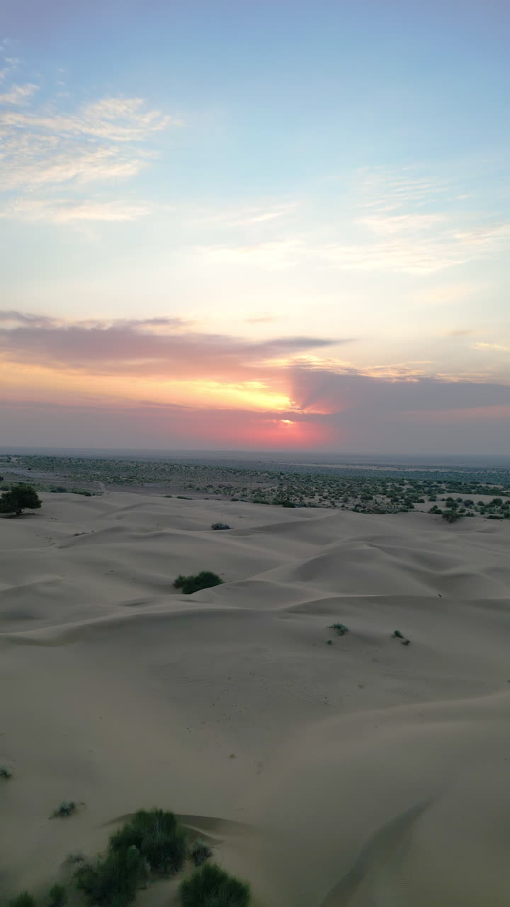 un dron captura una vista vertical de una vasta duna de arena en jaisalmer, rajasthan, durante la puesta del sol. las arenas doradas se extienden, con arbustos esparcidos 4k