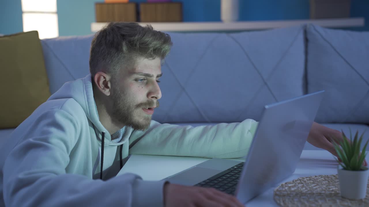 Bored depressed young man using laptop at home. Reluctant mood.