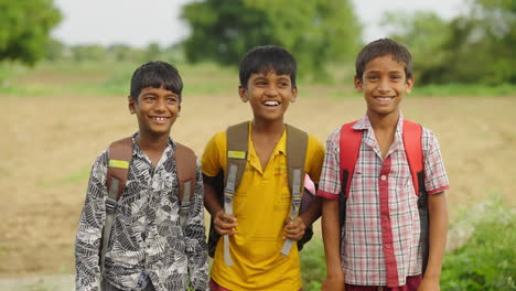 three smiling school children with backpacks in rural india