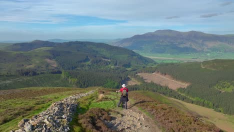 Mountain-walker-stopped-on-mountainside-path-enjoying-the-view-of-mountains-and-valleys-below-at-golden-hour