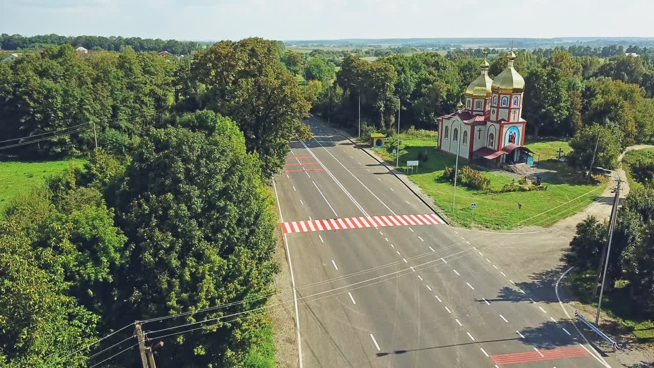 Aerial view of a new asphalt road. Flight over the highway surrounded by green trees in summer. Beautiful church near the road in the countryside.