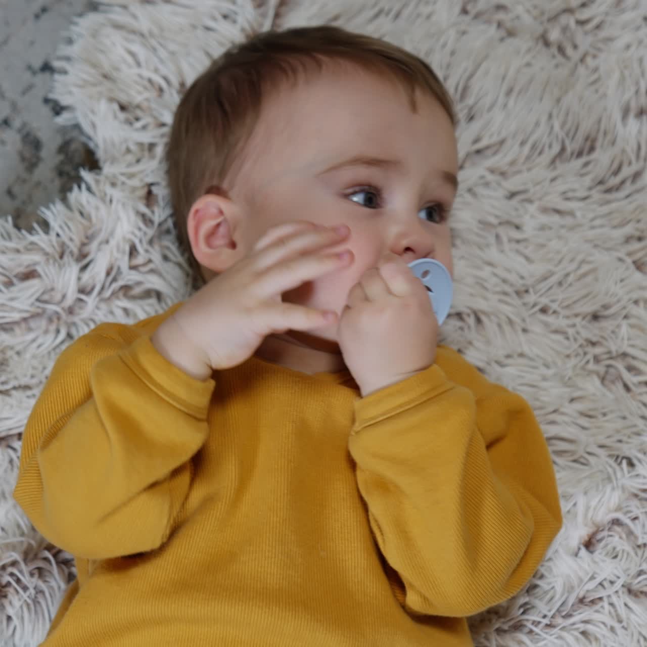 Lovely child lies peacefully on the fluffy plaid. Mom's hand gives him a pacifier and baby puts it into mouth. Top view