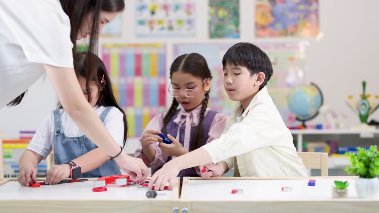 明るくモダンな理科の教室で、3人の小学生が先生に手伝ってもらいながらカラフルな磁石を研究しています。