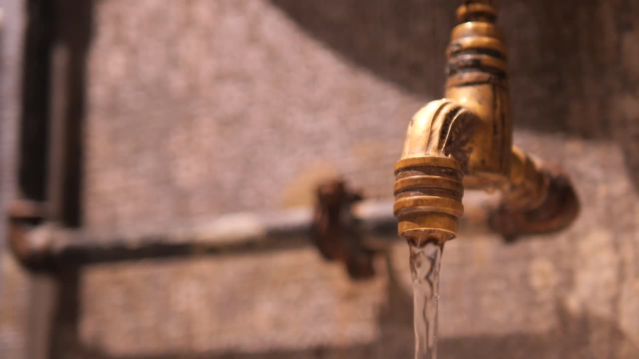 Primo piano di un vecchio rubinetto in ottone con acqua corrente