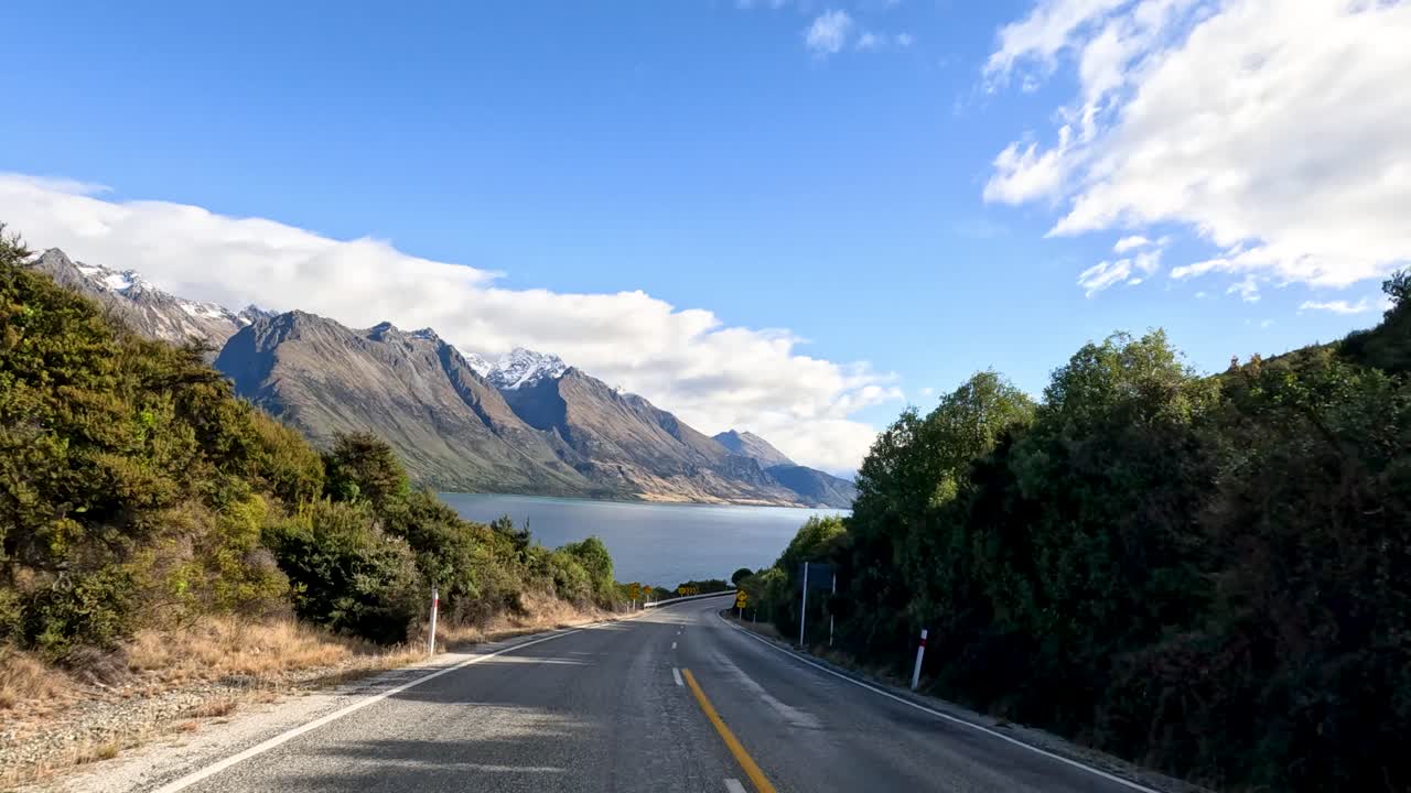 A picturesque drive through Queenstown's mountain roads, showcasing stunning lake views and lush greenery under clear skies