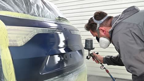 Spraying-trunk-of-blue-vehicle-by-professional-painter-with-protective-equipment