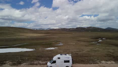 Aerial-circle-pan-of-a-white-camper-van-in-a-snowy-plateau,-Montenegro