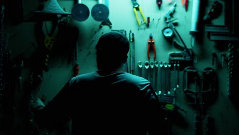 el hombre alcanza herramientas en una pared de taller débilmente iluminada.