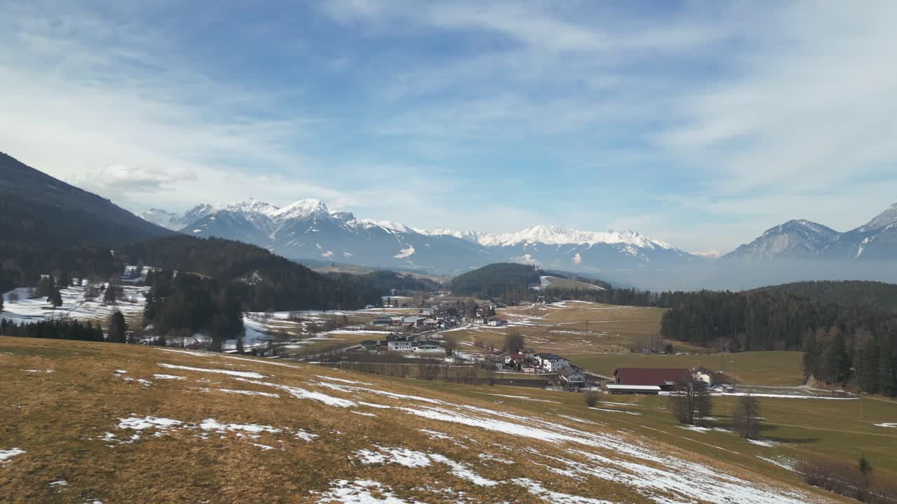 drones aéreos volando sobre campos de hierba marrón con pequeñas partes cubiertas de nieve y una carretera con bosques y casas