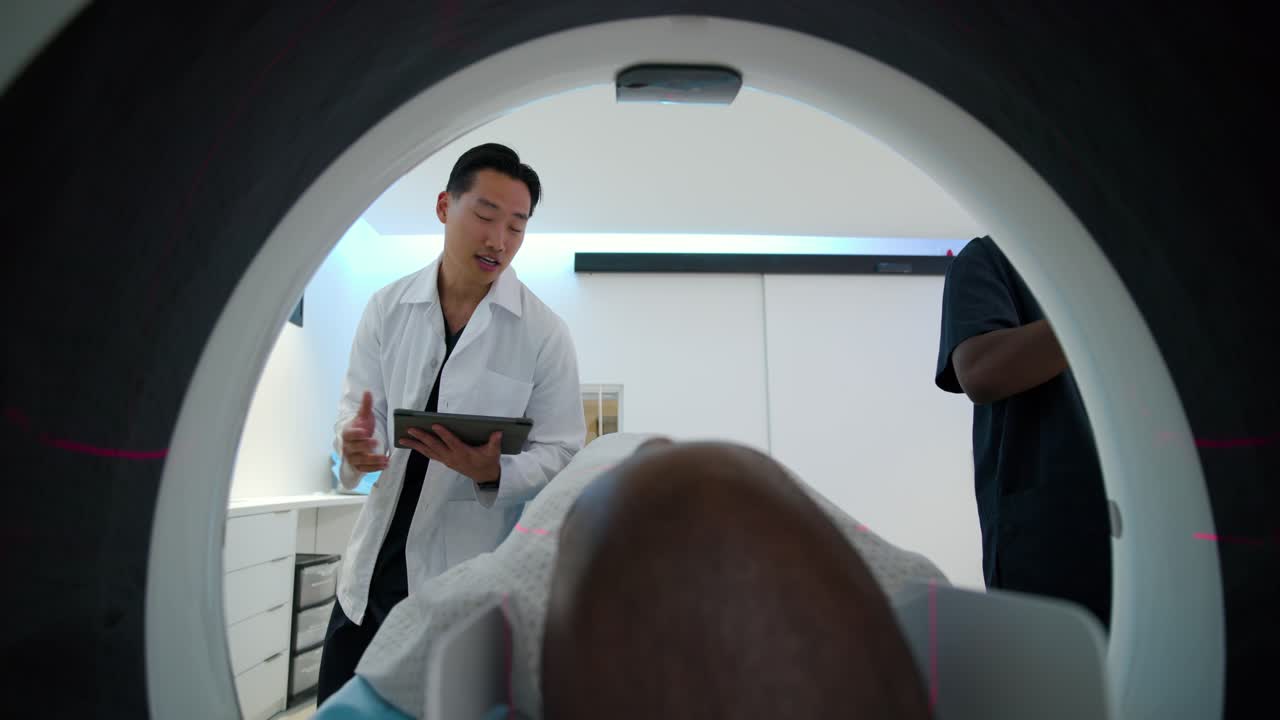 Un medico guida una paziente afroamericana all'interno del foro dello scanner nella sala TAC, toccando un tablet e fornendo spiegazioni