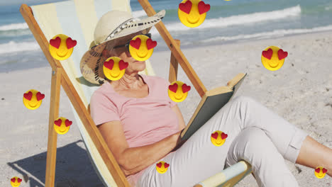 Animation-Von-Digitalen-Symbolen-Mit-Roten-Herz-Liebes-Emojis-über-Einer-Frau,-Die-Im-Liegestuhl-Am-Strand-Ein-Buch-Liest