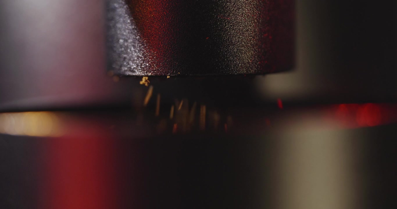 Macro, slow motion shot of coffee grounds coming out of an esthetic, professional coffee grinder in dramatic studio light